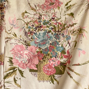 May include: A beige fabric with a floral pattern. The flowers are in shades of pink, blue, and green. The fabric has a vintage look.