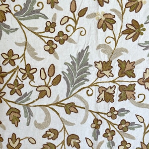 May include: A white fabric with embroidered floral designs in shades of brown and green. The floral pattern features leaves, flowers, and vines.