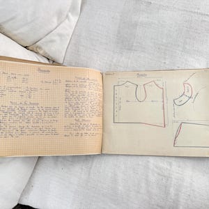 May include: An open notebook with grid paper pages featuring handwritten French text and technical sewing pattern illustrations. The left page contains detailed instructions, while the right page displays diagrams of garment pieces with measurements.