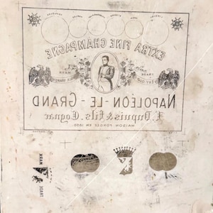 May include: A vintage champagne label with the text "EXTRA FINE CHAMPAGNE" and "NAPOLEON - LE-GRAND". The label features an illustration of Napoleon Bonaparte, eagles, and decorative circular elements. The label is aged and has a distressed appearance.