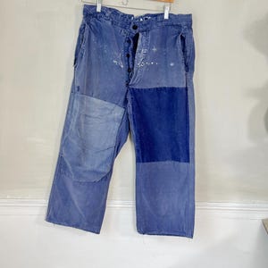 May include: Blue denim pants with multiple patches sewn on. The patches are different shades of blue and are sewn in a patchwork style.