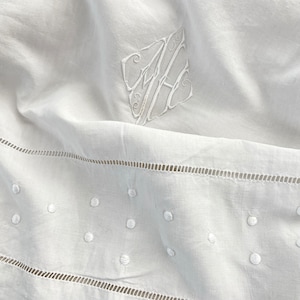 Puede incluir: Mantel de mesa de lino blanco con lunares blancos bordados y un monograma en la esquina superior izquierda.