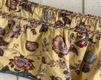 Könnte beinhalten: Ein gelber Stoff-Vorhang mit einem floralen Muster in Rot-, Rosa- und Blautönen. Der Vorhang hat einen blauen Saum und ein geflochtenes Kordeldetail.