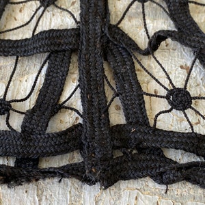 May include: Close-up of black braided rope woven into a intricate pattern. The rope is thick and textured, creating a detailed design.