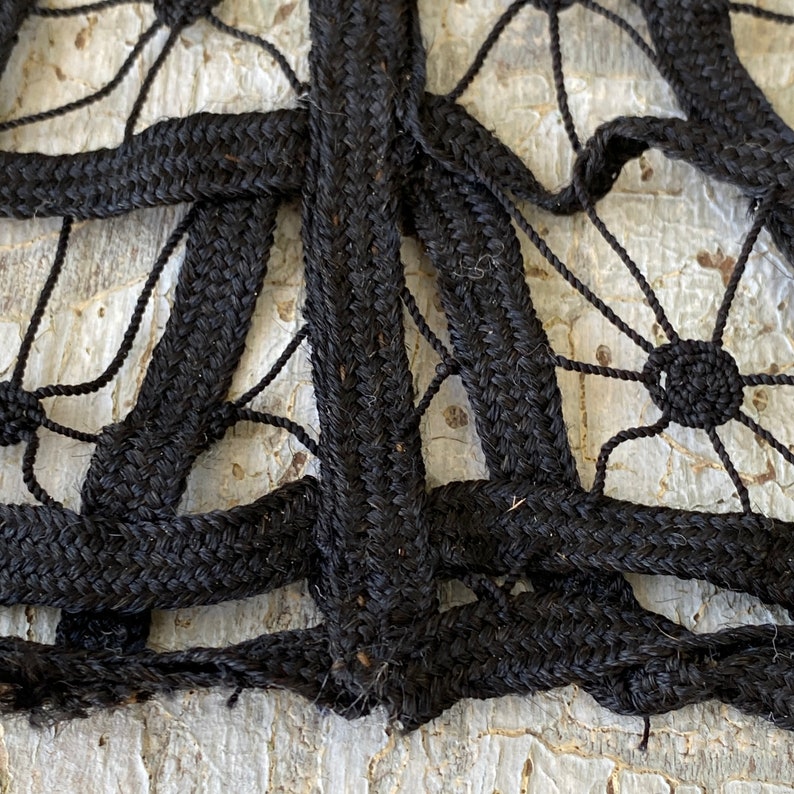 May include: Close-up of black braided rope woven into a intricate pattern. The rope is thick and textured, creating a detailed design.