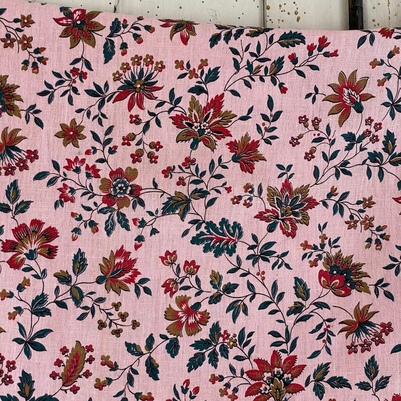 May include: Pink fabric with a repeating floral pattern. The flowers are in shades of red, brown, and green. The fabric has a linen texture.