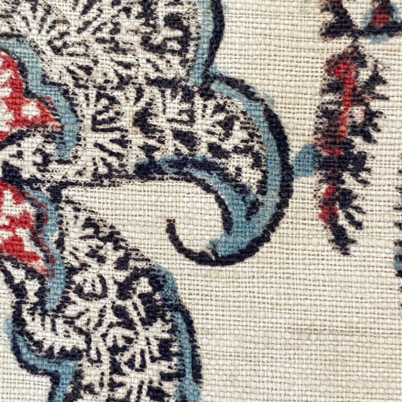 Pu&ograve; includere: Primo piano di un tessuto con un motivo paisley in tonalit&agrave; di blu, nero e rosso su uno sfondo beige.