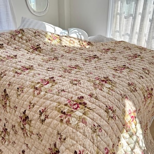 Op de afbeelding: Een beige bloemenquilt met een gestikt patroon. De quilt is gemaakt van een zachte, lichte stof en heeft een delicaat bloemenontwerp in roze, groene en bruine tinten.