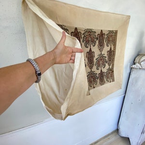 Pu&ograve; includere: Un arazzo da parete in tessuto color crema con un motivo paisley in tonalit&agrave; di rosso, nero e verde. Il tessuto &egrave; ripiegato per rivelare il retro semplice color crema.