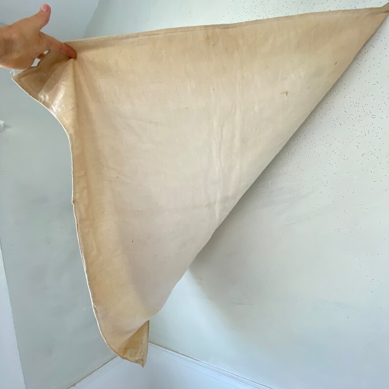 Pu&ograve; includere: Un telo di tela bianca semplice, piegato a met&agrave;, con una mano che tiene l'angolo del telo.