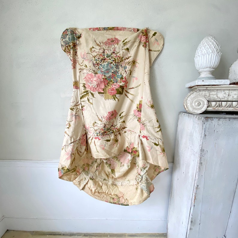 May include: A white floral fabric chair slipcover with a ruffled hem and a floral pattern in shades of pink, green, and blue.