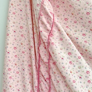 May include: Pink fabric with a small floral print and a ruffled edge. The fabric is folded in half, with the ruffled edge on the outside.