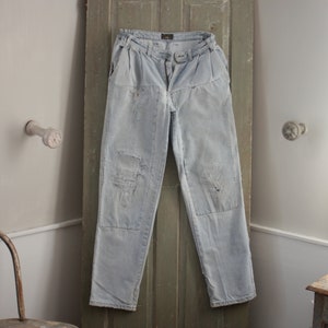 May include: A pair of light blue denim trousers with multiple patches and visible wear and tear. The trousers have a high waist and a straight leg.