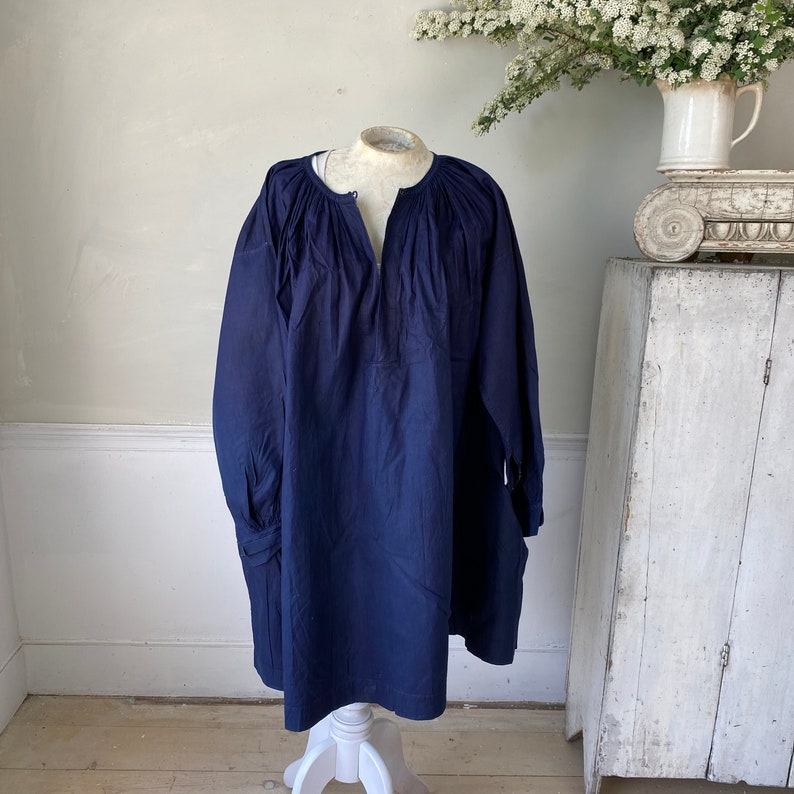 May include: A navy blue tunic top with a gathered neckline and long sleeves. The top is made of a soft, lightweight fabric and has a relaxed fit.