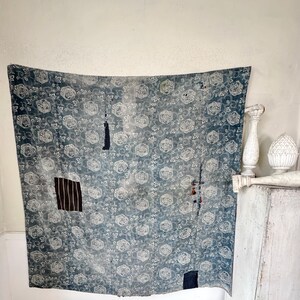 May include: A blue and white floral patterned fabric with patches of different fabrics sewn on. The fabric is hanging on a white wall.