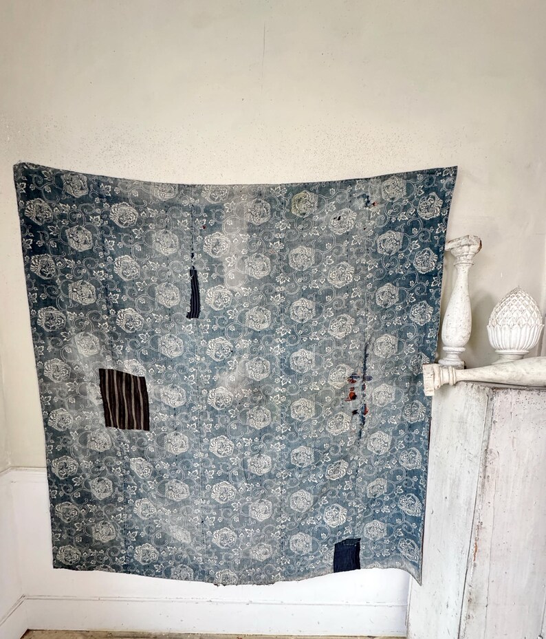 May include: A blue and white floral patterned fabric with patches of different fabrics sewn on. The fabric is hanging on a white wall.