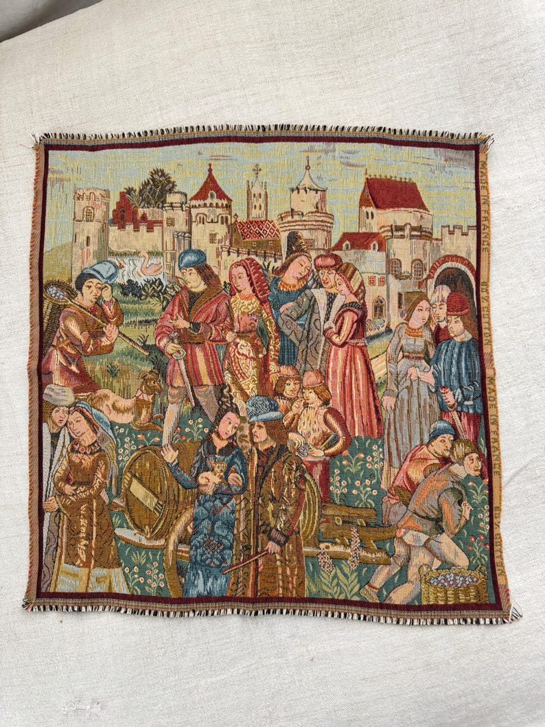 May include: A woven tapestry depicting a medieval scene with figures in period clothing, set against a backdrop of castles and buildings. The tapestry features a border and the text "MADE IN FRANCE".