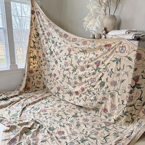 Puede incluir: Una tela grande de color crema con un patrón floral en tonos de rosa, azul y verde. La tela está drapeada sobre una superficie y parece ser un mantel o una colcha.