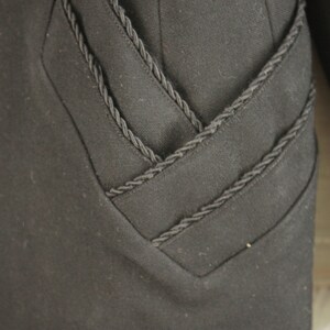 May include: Black blazer with a decorative braided trim detail on the front and sleeves.