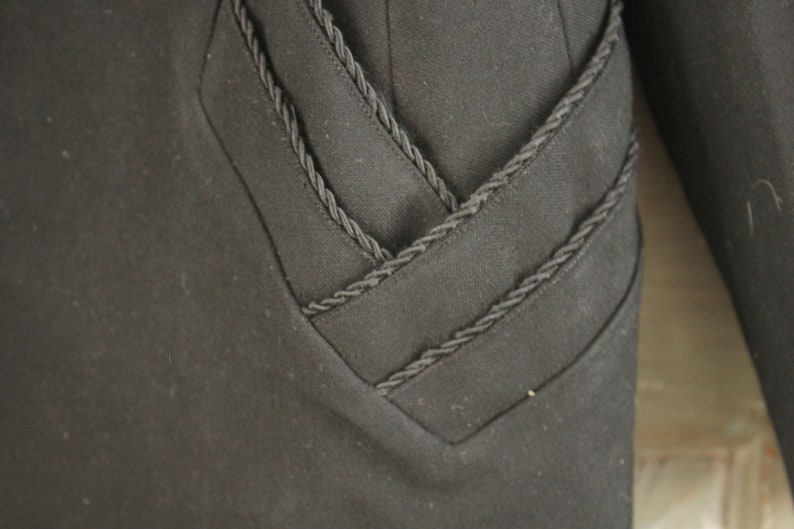 May include: Black blazer with a decorative braided trim detail on the front and sleeves.