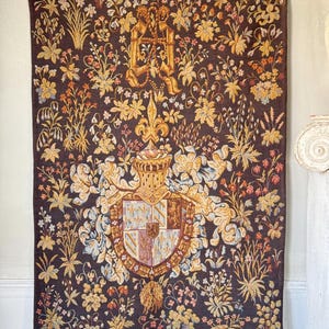 May include: A large tapestry with a dark brown background, featuring a detailed floral pattern in shades of gold, yellow, and pink. The central design includes a coat of arms with a crown and fleur-de-lis.