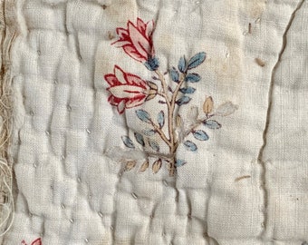 Puede incluir: Primer plano de una tela blanca con un patrón floral. La tela está acolchada y tiene un aspecto desgastado y vintage. Las flores son rojas, azules y marrones.