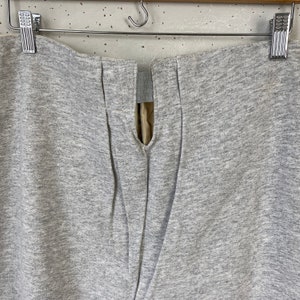 Pode incluir: Cal&ccedil;as de moletom cinzas com uma costura central nas costas e um fecho de correr.