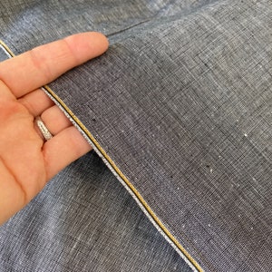 May include: Close-up of a dark gray fabric with a subtle texture. The fabric has two thin yellow lines running along the edge.
