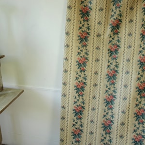 K&ouml;nnte beinhalten: Ein Vintage-Blumenstoff mit einem sich wiederholenden Muster aus rosa Bl&uuml;ten und gr&uuml;nen Bl&auml;ttern auf cremefarbenem Hintergrund. Der Stoff hat ein dezentes Karomuster.