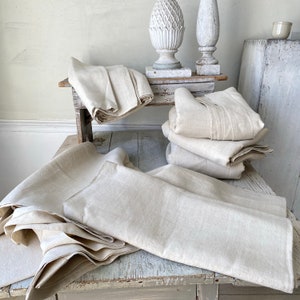 May include: A stack of off-white linen fabric on a wooden table. The fabric is folded and has a natural, rustic look.