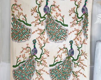 May include: A white fabric with a repeating pattern of peacocks with green, pink, and gray feathers. The peacocks are perched on branches with pink blossoms.