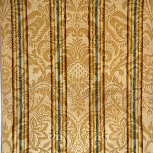 Könnte beinhalten: Nahaufnahme eines gemusterten Stoffes mit einem Damastmuster in Gold- und Beigetönen. Vertikale Streifen in Braun und Grau verlaufen über den Stoff. Der Stoff hat ein weiches, strukturiertes Aussehen, geeignet für Polster oder dekorative Zwecke.