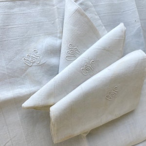 May include: Four white linen handkerchiefs with embroidered initials. The handkerchiefs are folded and stacked on top of each other.