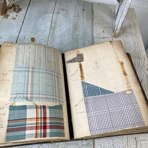 May include: An open book with fabric swatches attached to the pages. The swatches are various shades of blue and white plaid, with some having a red stripe. The book has handwritten numbers and text on the pages, including "Type 311", "Remnant 314", and "52112".