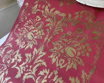 May include: A roll of red wallpaper with a gold floral damask pattern. The design features large, ornate flowers and scrolling leaves. The wallpaper is partially unrolled, revealing the intricate details of the classic design.