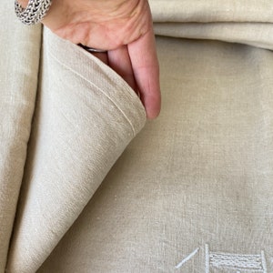 May include: A close-up of a natural linen tablecloth with a subtle texture. The fabric is folded over, revealing the underside of the cloth.