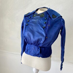 May include: A vintage cobalt blue jacket with long sleeves and a double-breasted design. The jacket features decorative buttons and embroidered accents on the collar. The waist is cinched, and the jacket is displayed on a mannequin.