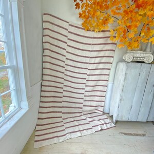 May include: A large, striped throw blanket with a cream background and red stripes. The blanket is folded and draped over a white surface.