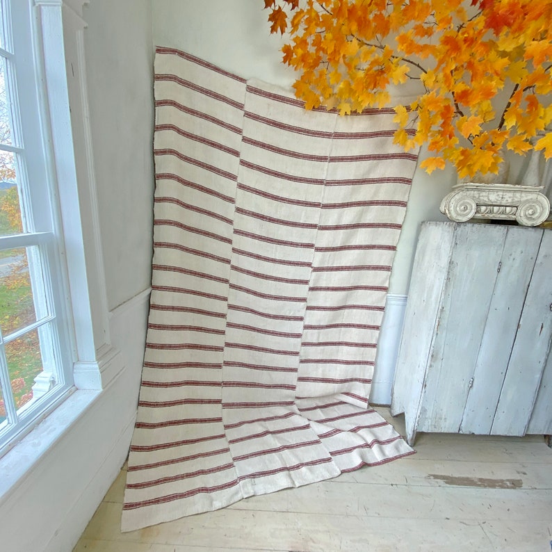 May include: A large, striped throw blanket with a cream background and red stripes. The blanket is folded and draped over a white surface.