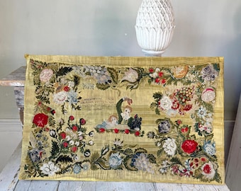 May include: Antique embroidered textile with floral and figure details. The textile features a yellow background with a striped pattern, and is framed by a border of colorful flowers. The text reads "And live forever..." and depicts two children.