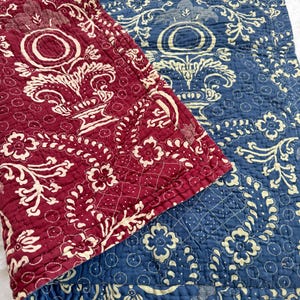 May include: A quilted fabric with a floral pattern in shades of red and blue. The fabric is folded in half, revealing both sides of the pattern.