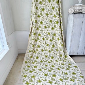 May include: A white fabric with a green and light green grapevine pattern. The fabric is draped over a white surface.