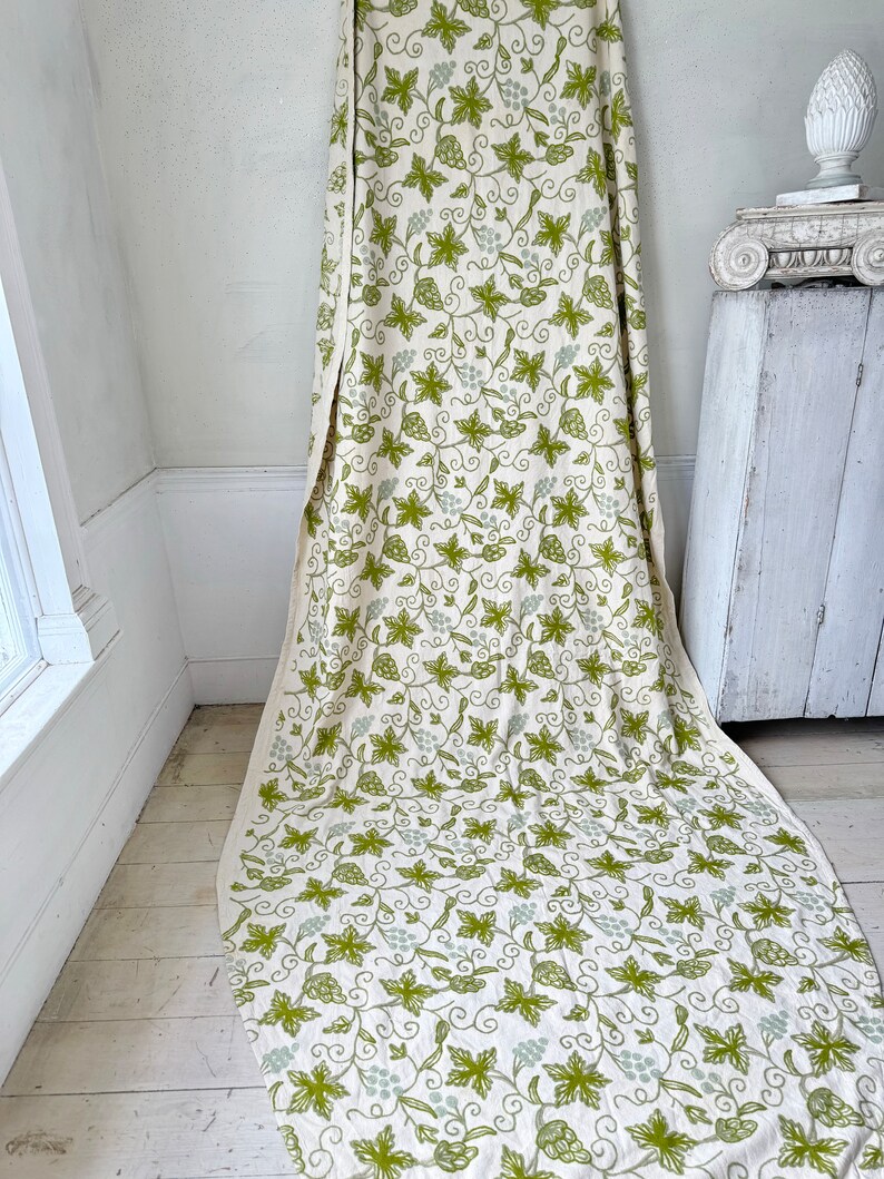 May include: A white fabric with a green and light green grapevine pattern. The fabric is draped over a white surface.