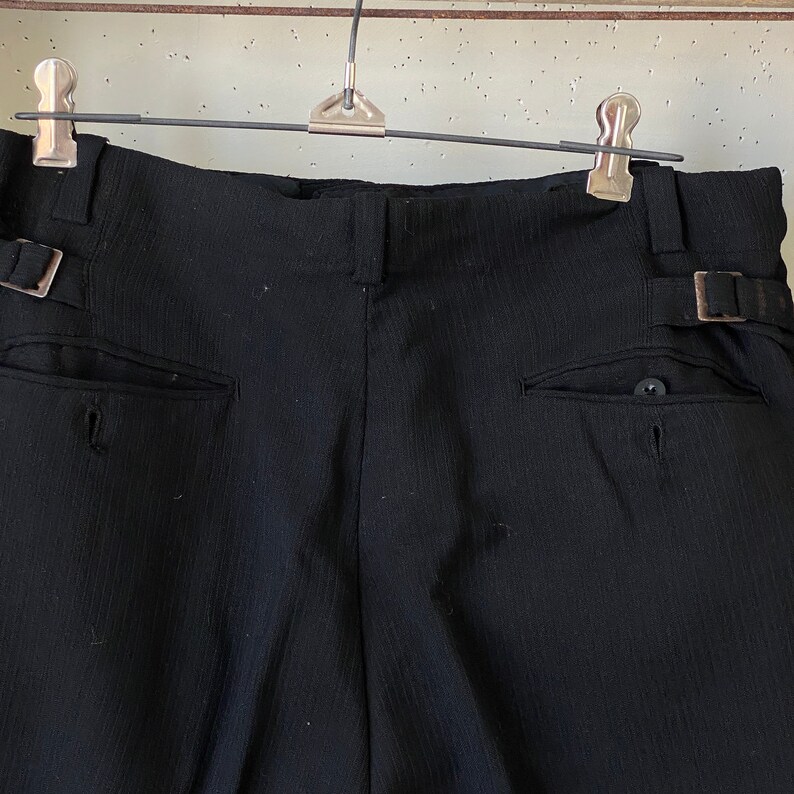 May include: Black pinstripe pants with a belt loop and a button on the back pocket.