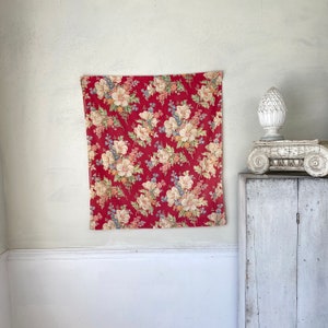 Könnte beinhalten: Ein rotes Stoffpanel mit einem floralen Muster mit weißen, rosa und blauen Blumen. Der Stoff ist im Vintage-Stil mit leicht verblassten Farben.