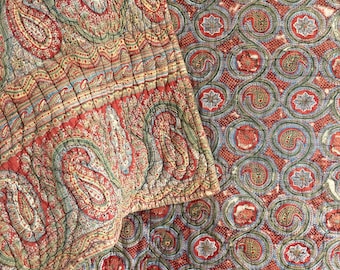 Puede incluir: Una colcha de tejido acolchado con estampado paisley rojo y verde. La colcha está doblada por la mitad, mostrando ambos lados de la tela.