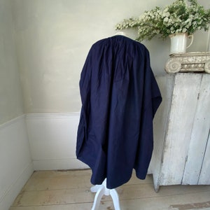 May include: A navy blue, loose-fitting, long tunic-style top with a gathered neckline. The top is made of a soft, drapey fabric and is hanging on a white stand.