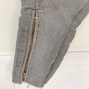 May include: Close-up of a gray ribbed fabric with a gold zipper running down the side. The fabric has a slight fray at the bottom edge.