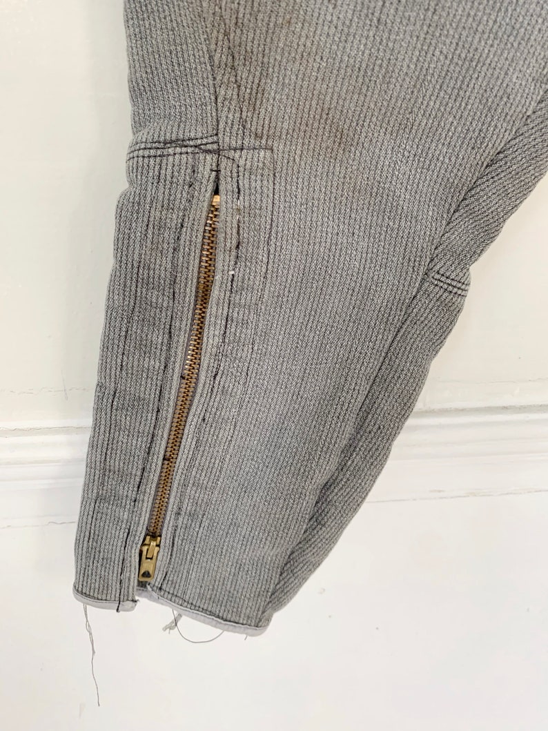 May include: Close-up of a gray ribbed fabric with a gold zipper running down the side. The fabric has a slight fray at the bottom edge.
