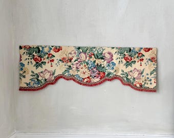 Könnte beinhalten: Ein floraler Fensterbehang mit cremefarbenem Hintergrund und einem lebendigen Muster aus roten, rosa, lila und blauen Blumen. Der Fensterbehang hat einen gewellten Rand mit roter Fransen und silberner Zierleiste.